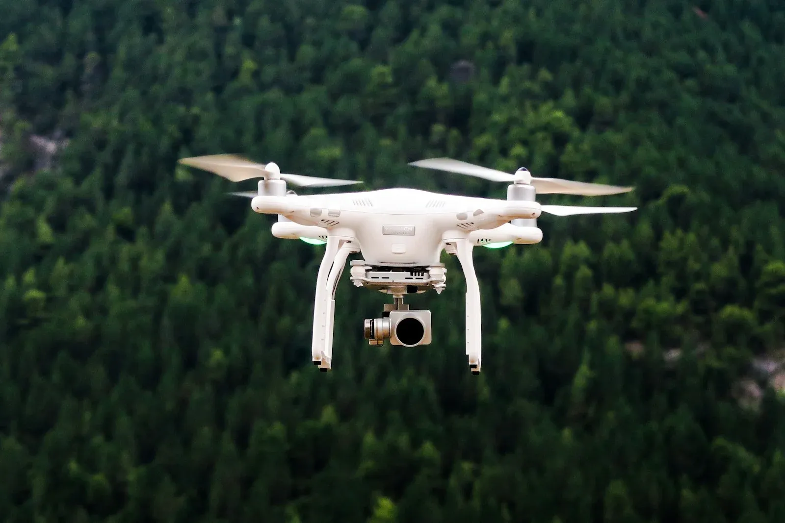 A white quadcopter drone flying in front of a wooded hillside